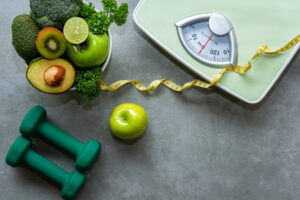 weight loss resolution- scale, weights, and bowl of green fruit